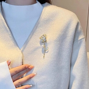 Détail de la broche rose avec cristaux et perle sur un pull en maille beige
