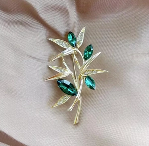 Macro detail of golden bamboo brooch with dark green gemstones and crystal rhinestones