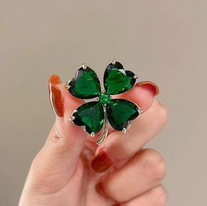 Elegant silver four-leaf clover brooch featuring sparkling emerald green heart crystals