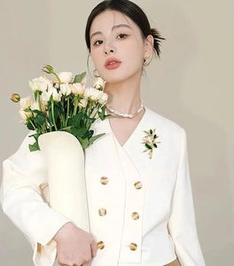 Detail of luxury green bamboo branch brooch pinned on a white double-breasted blazer lapel