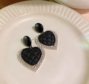 Detailed macro view of heart-shaped drop earrings featuring black quilted leather and crystals