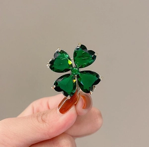 Detailed close-up of emerald clover brooch featuring heart-shaped crystals in gold setting