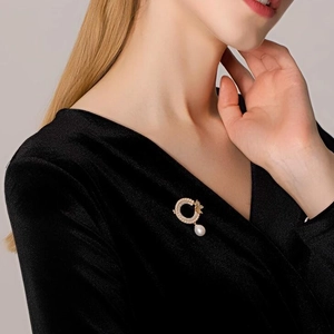 Broche élégante en forme d'anneau doré avec perle et strass portée sur un vêtement noir