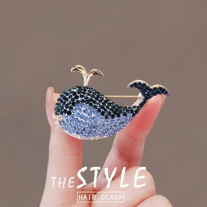 Elegant gold whale brooch with blue gradient rhinestones held by a model