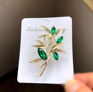 Detailed close-up of a luxury gold bamboo brooch with green marquise crystals