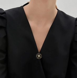 Close-up of black camellia brooch with gold edges and a pearl on a black V-neck top