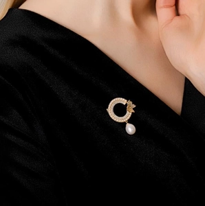 Vue détaillée d'une élégante broche dorée avec motifs de feuilles et perle pendante