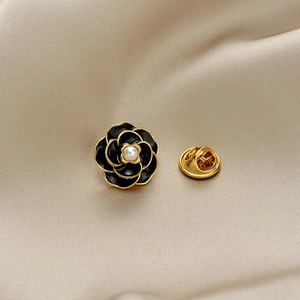 Close-up of black camellia enamel brooch with gold trim and white pearl center