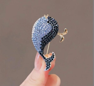 Detail view of blue rhinestone whale brooch with gold accents held in hand