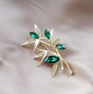 Detail of bamboo brooch with emerald green crystal leaves and gold branch design