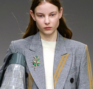Detailed view of luxury gold bamboo leaf brooch with green gems on a grey blazer