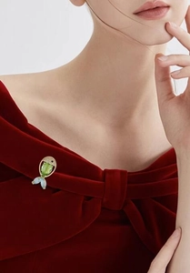 Edle goldene Fischbrosche mit grünem Kristall auf einem roten Samtkleid an der Schulter