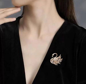 Sparkling swan brooch in gold finish with white crystals on elegant black velvet dress