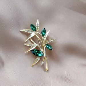 Macro detail of luxury bamboo leaf brooch with green gemstones and sparkling crystals