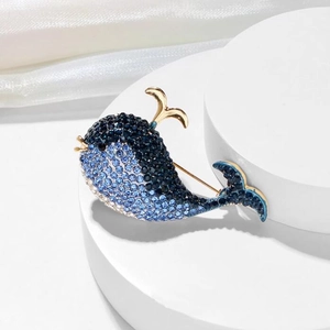 Detail of blue rhinestone whale brooch with gold accents on a white display stand