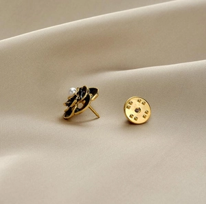 Detailed close-up of a black flower brooch with a central pearl on beige satin fabric