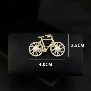 Close-up of golden bicycle brooch with sparkling rhinestones and white pearls on wheels