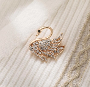 Elegant gold swan brooch with sparkling crystals on white knitwear clothing