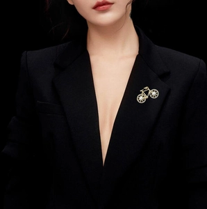 Close-up of a golden bicycle brooch with pearl wheels pinned on a black suit jacket