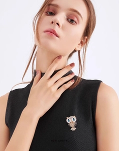 Detail shot of a cute owl brooch with blue eyes and white enamel on a black vest