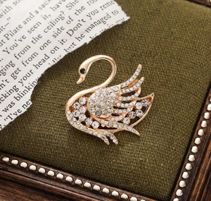 Detailed view of a gold swan brooch featuring sparkling rhinestones on a dark green box