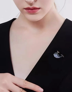Detailed view of the sparkling blue whale brooch pinned on a black v-neck suit jacket