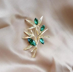 Detail of bamboo brooch with green marquise gems and diamonds on silk background