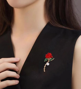 Élégante broche rose émaillée rouge avec feuilles vertes et perle sur vêtement noir