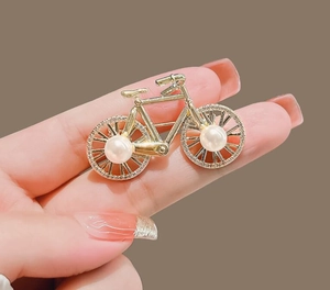 Close-up of golden bicycle brooch featuring sparkling rhinestones and pearl wheels