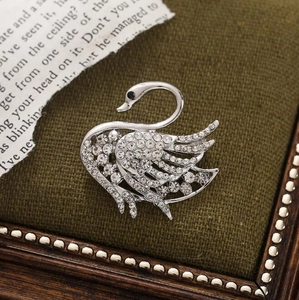 Macro shot of silver swan brooch featuring sparkling crystal inlay on green fabric