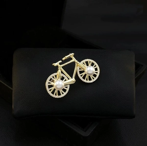 Macro detail of bicycle brooch with gold metal frame, pearl wheels and white rhinestones