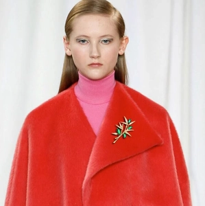 Luxury gold branch brooch with olive green gems worn on a stylish red plush coat