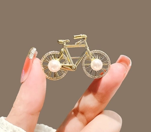 Close-up of a gold bicycle brooch with white pearls and sparkling rhinestone details