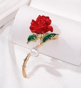 Détail d'une broche rose émaillée rouge avec feuilles vertes, tige dorée et perle blanche