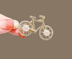 Close-up of a gold bicycle brooch with white pearls and sparkling zircon accents on wheels