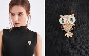 Detail of owl brooch featuring blue crystal eyes and pavé stones on a black fabric