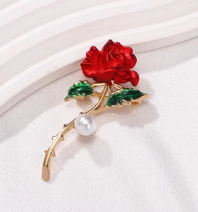 Détail macro d'une broche rose en émail rouge avec feuilles vertes et perle blanche