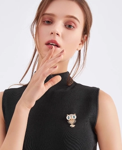 Detailed view of an owl brooch with blue stones and white enamel on a black sweater