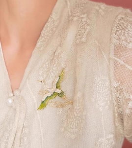Close-up of crane brooch with green enamel wings and zircon inlay on lace outfit