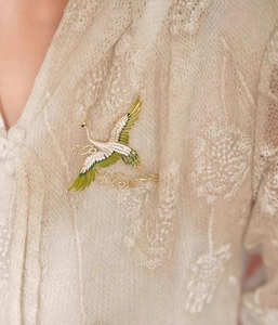 Detailed view of an elegant flying crane brooch with green enamel and white zircons