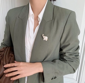 Detail view of a cute ivory elephant brooch with gold trim on a green suit lapel