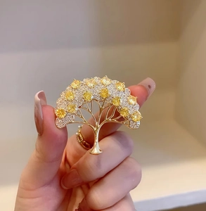 Dettaglio della spilla a ginkgo dorata con zirconi bianchi e pietre gialle lucide