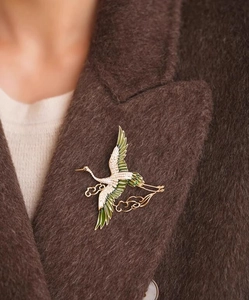 Detail of elegant crane brooch with green enamel wings on a dark wool coat lapel