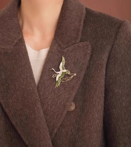 Detail of crane brooch with green enamel wings and white crystals on a wool coat