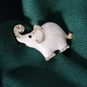 Close-up of a cute elephant brooch with creamy enamel and rhinestones on green fabric