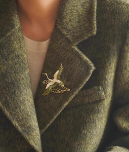 Detail of elegant gold crane brooch with enamel wings pinned on a green tweed wool coat lapel