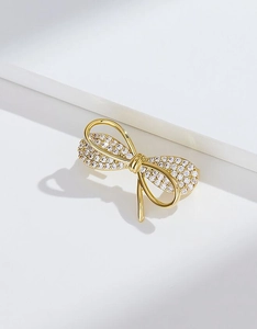 Gros plan sur l'élégante broche nœud dorée avec cristaux brillants sur fond blanc