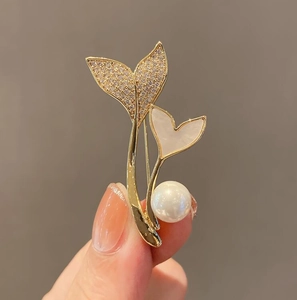 Detailed close-up of a whale tail brooch with sparkling crystals and a white pearl