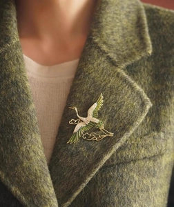 Detail shot of a golden crane brooch with green enamel on a dark wool coat