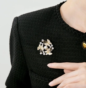 Detailed close-up of a gold butterfly pearl brooch pinned on a black textured tweed jacket